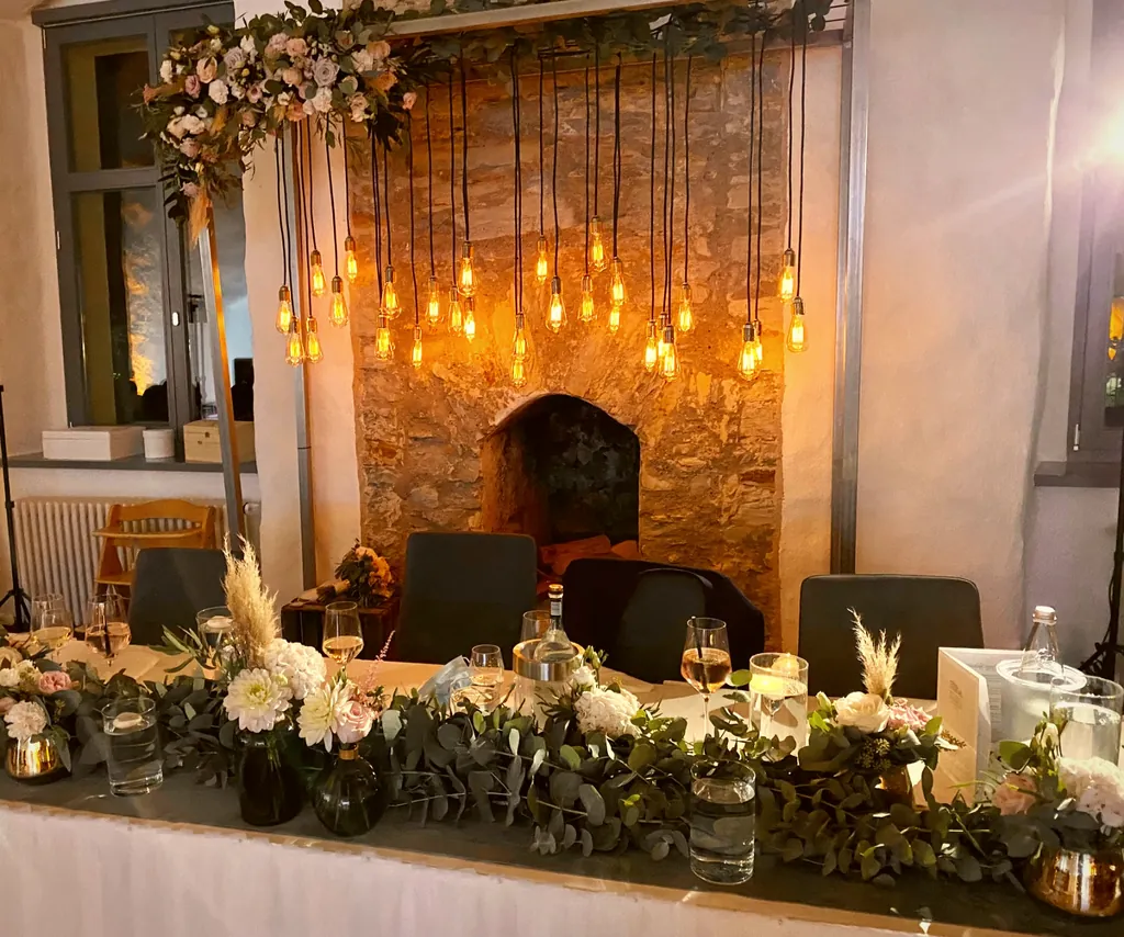 Brauttisch mit warmer Gluehbirnen-Lichterkette ueber Tafeldekoration