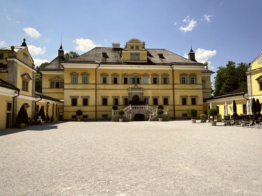 Schloss Hellbrunn in Salzburg bei Sonnenschein, gelbe Barockfassade vor blauem Himmel Schloss Hellbrunn in Salzburg bei Sonnenschein, gelbe Barockfassade vor blauem Himmel