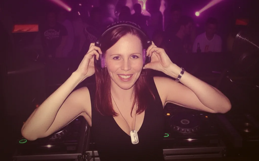 Sabrina Blömer lächelnd mit Kopfhörern am Pioneer-Pult, Partycrowd im Hintergrund