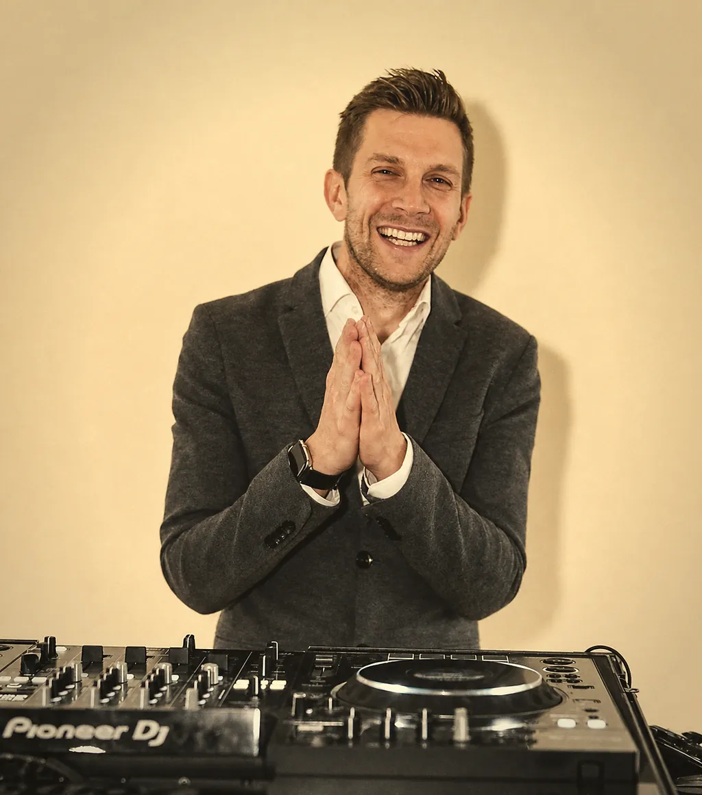 DJ René Büker lächelnd hinter dem Pioneer-DJ-Pult, Design-R-Music