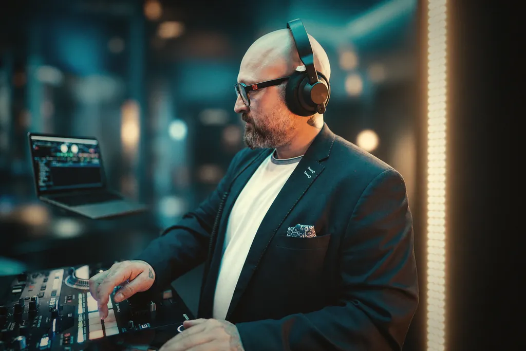 DJ Janni de Luxe im Sakko mit bronzefarbenen Kopfhörern am Pult, Studio-Setting DJ Janni de Luxe im Sakko mit bronzefarbenen Kopfhörern am Pult, Studio-Setting