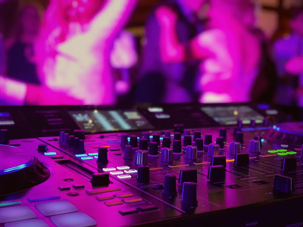Pioneer-DJ-Pult mit Mixer vor tanzender Menge in magentafarbenem Licht