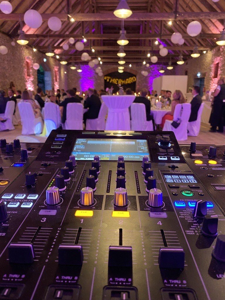 DJ-Pult mit Pioneer-Setup im Eventraum Wasserschloss Thienhausen, Steinmauern, Holzbalkendecke und Lampions über weißen Tischrunden DJ-Pult mit Pioneer-Setup im Eventraum Wasserschloss Thienhausen, Steinmauern, Holzbalkendecke und Lampions über weißen Tischrunden