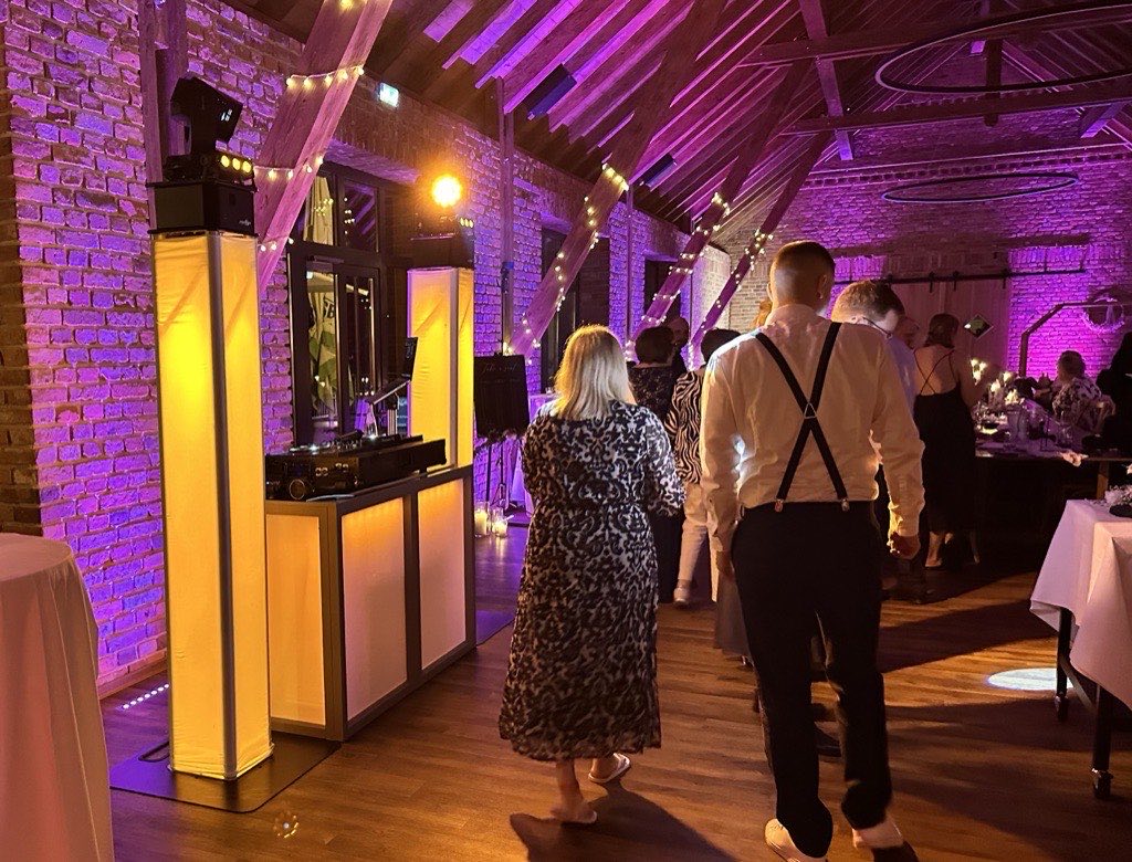 Festscheune Königshof Bielefeld bei Hochzeitsabend mit magentafarbener Wandbeleuchtung, Lichterkette-Sternenhimmel und beleuchtetem DJ-Setup vor Ziegelmauer Festscheune Königshof Bielefeld bei Hochzeitsabend mit magentafarbener Wandbeleuchtung, Lichterkette-Sternenhimmel und beleuchtetem DJ-Setup vor Ziegelmauer