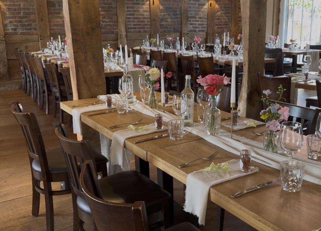 Lange Hochzeitstafel im Hofrestaurant von Laer Herford mit eingedeckten Holztischen, Kerzen und Pastell-Blumengestecken vor Ziegelmauer Lange Hochzeitstafel im Hofrestaurant von Laer Herford mit eingedeckten Holztischen, Kerzen und Pastell-Blumengestecken vor Ziegelmauer