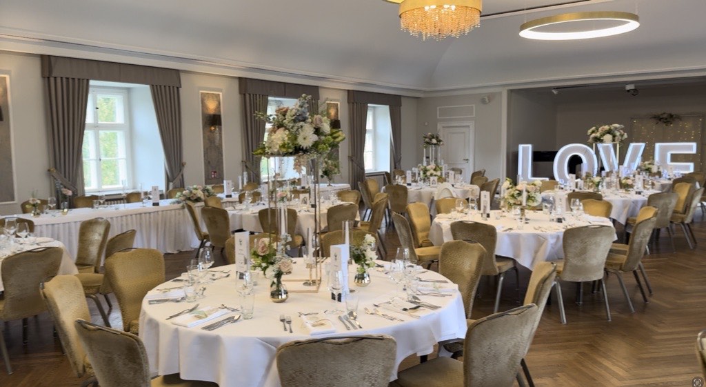 Festsaal Schloss Ovelgönne Bad Oeynhausen mit eingedeckten weißen Hochzeitstafeln, goldenen Stühlen, hohen Blumenarrangements und beleuchtetem LOVE-Schriftzug Festsaal Schloss Ovelgönne Bad Oeynhausen mit eingedeckten weißen Hochzeitstafeln, goldenen Stühlen, hohen Blumenarrangements und beleuchtetem LOVE-Schriftzug