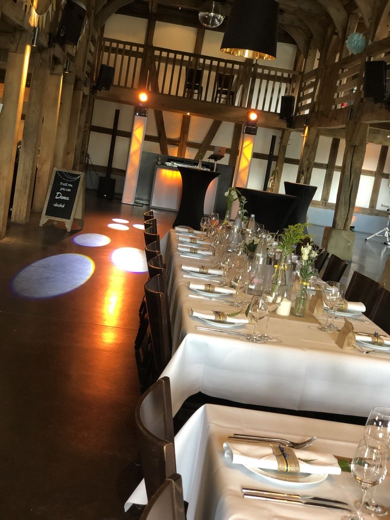 Eventscheune Gut Lippesee Paderborn mit Holzbalken-Decke, Galerie-Empore, eingedeckter Hochzeitstafel und warm beleuchtetem DJ-Setup mit Bodenlichtern Eventscheune Gut Lippesee Paderborn mit Holzbalken-Decke, Galerie-Empore, eingedeckter Hochzeitstafel und warm beleuchtetem DJ-Setup mit Bodenlichtern